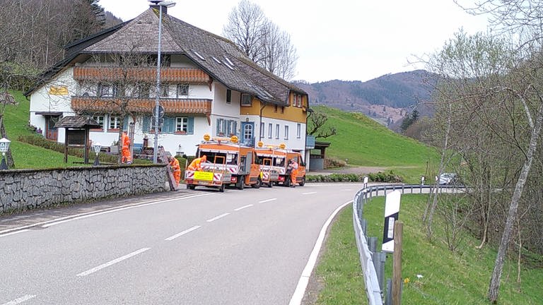 Landstraße mit Straßenarbeitern und orangem Fahrzeug, Anbringung von Straßenschild
