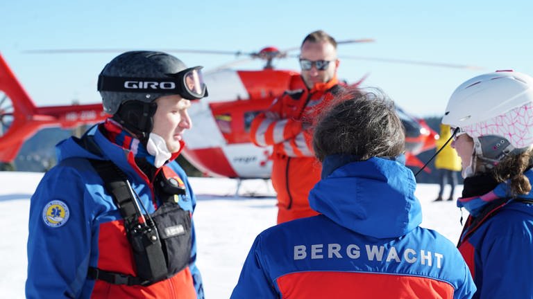 100-jähriges Jubiläum: Ein Pilot steht vor seinem Hubschrauber und wartet darauf, dass eine von der Bergwacht gerettete Person abtransportiert werden kann. (Foto: SWR)