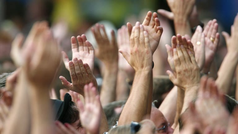 Menschen strecken bei einem Konzert ihre Hände in die Luft und klatschen. (Foto: picture-alliance / Reportdienste, picture-alliance/ dpa | Rolf Haid)