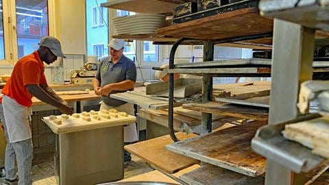 Die Bäckerei in der Abdoulie arbeitet ist zu sehen. Er rollt Teig und man sieht einige Regale für die Backwaren. (Foto: SWR, Jasmin Bergmann)