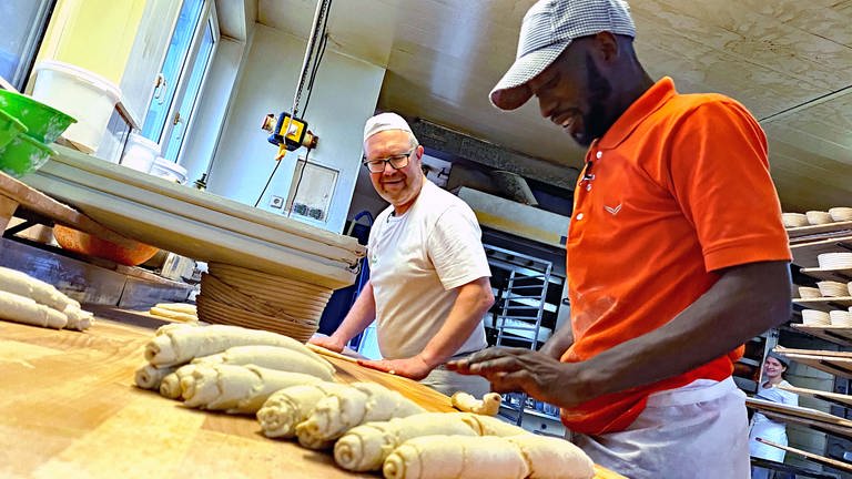 Mit seinen Händen rollt der Bäcker-Lehrling den Teig. Er und sein Lehrmeister strahlen.  (Foto: SWR, Jasmin Bergmann)