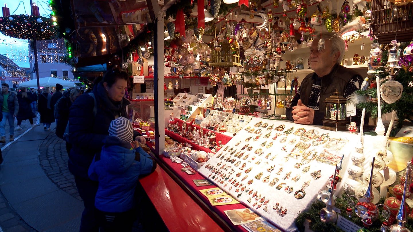 In einer Weihnachtsmarkt Bude hängen viele bunte Kugeln. Im inneren steht ein Mann mit wießen Jahren. (Foto: SWR)