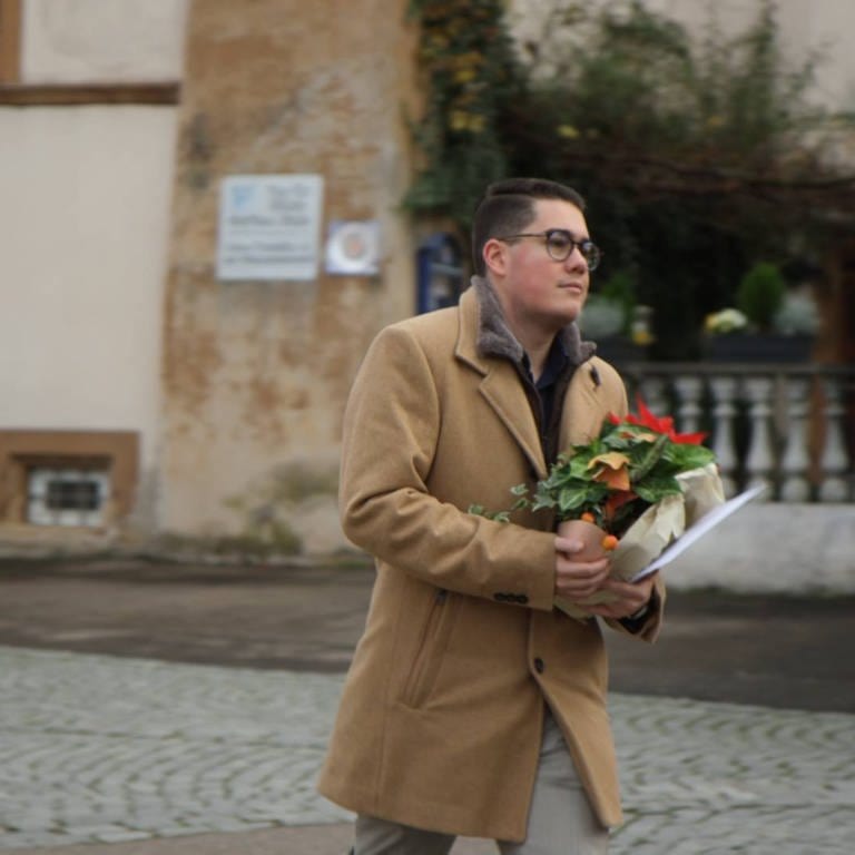 Mit einem Weihnachtsstern in der Hand geht Lukas Mahler in Pfaffenweiler (Landkreis Breisgau-Hochschwarzwald) in Richtung Rathaus. (Foto: SWR)