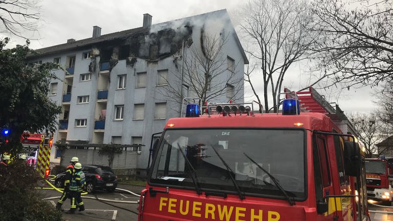 Ein hellblaues Mehrfamilienhaus in Offenburg ist zu sehen. Vier Fenster im obersten Stockwerk sind schwarz vor Ruß. Aus den Fenstern steigt Rauch auf. Vor dem Haus stehen mehrere Feuerwehrautos. (Foto: SWR, Ulf Seefeldt)
