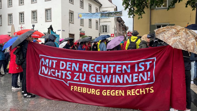 Menschen mit Regenschirmen hinter einem Plakat mit der Aufschrift "Mit den Rechten ist nichts zu gewinnen! Freiburg gegen Rechts". (Foto: SWR)
