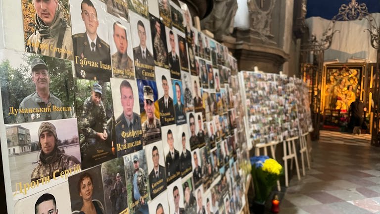 Fotowände mit vielen Bildern von Soldaten und einigen Frauen in einer Kirche.