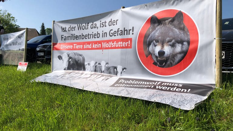 Ein Plakat an einem Zaun mit der Aufschrift: "Ist der Wolf da, ist der Familienbetrieb in Gefahr. Unsere Tiere sind kein Wolfsfutter."