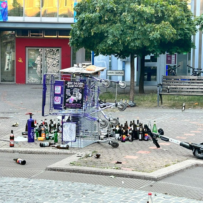 Zwei Einkaufswagen liegen umgekippt auf dem Lederleplatz, umgeben von leeren Flaschen und Müll. (Foto: Privat)