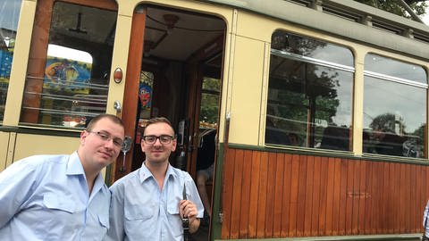 Zwei Männer vor einer nostalgischen beigefarbenen Straßenbahn.