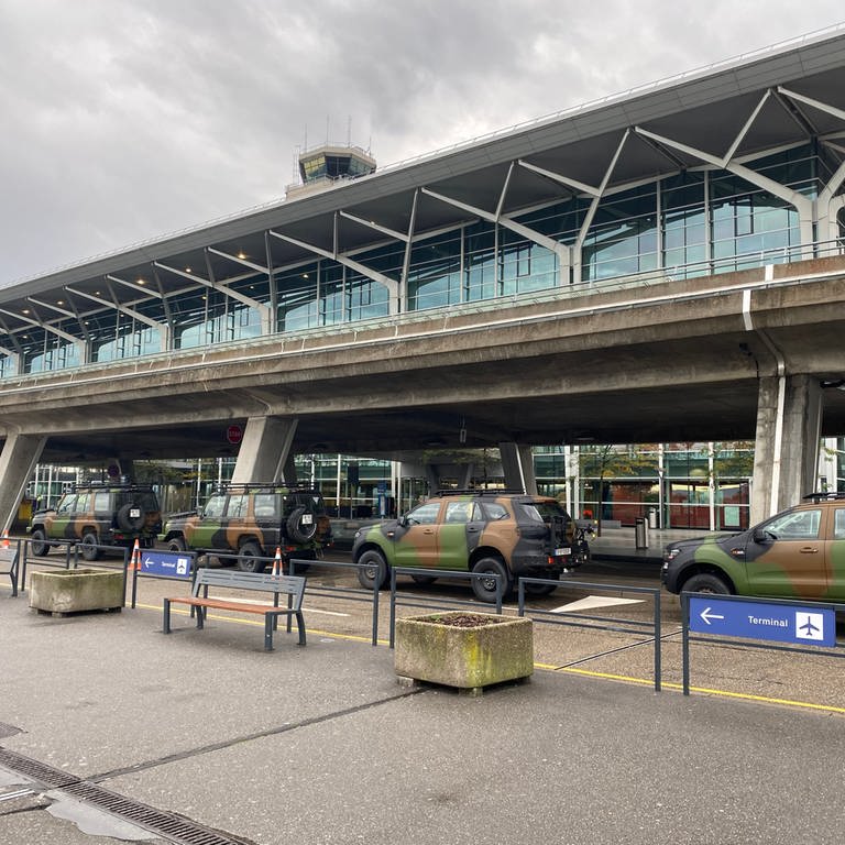 Geländewagen in Tarnfarben stehen auf der Straße vor dem Gebäude des Basler Flughafens.