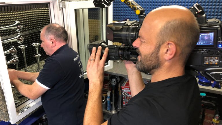 Ein Kameramann filmt einen Mann in einer Werkstatt