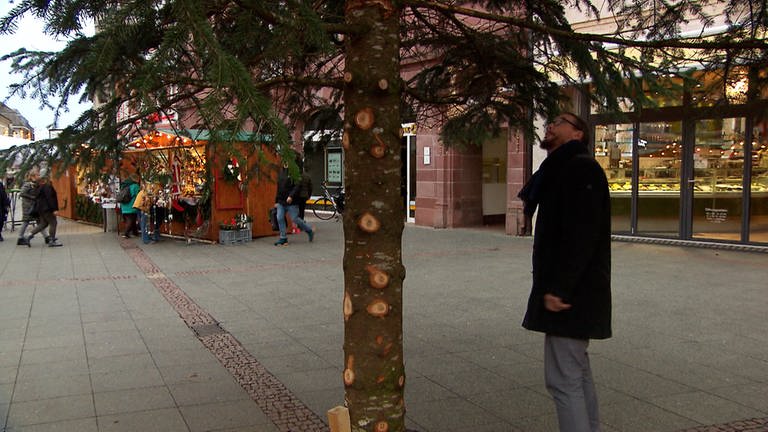 Ein Mann steht neben dem Weihnachtsbaum, dem die Äste abgeschnitten wurden. (Foto: SWR)
