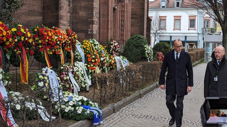 Mann mit Brille und dunklem Anzug steht neben den unzähligen Blumenkränzen, die vor der Stadtkirche aufgereiht wurden. (Foto: SWR, Thomas Hermanns)