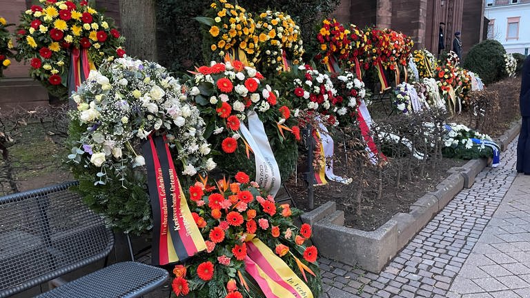 Viele Blumenkränze liegen vor der Stadtkirche, sie haben verschiedene Farben von weiß bis orange. (Foto: SWR, Christoph Ebner)