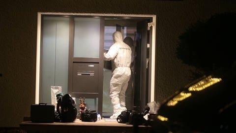 Ein Kriminaltechniker in einem weißen Schutzanzug betritt ein Haus.