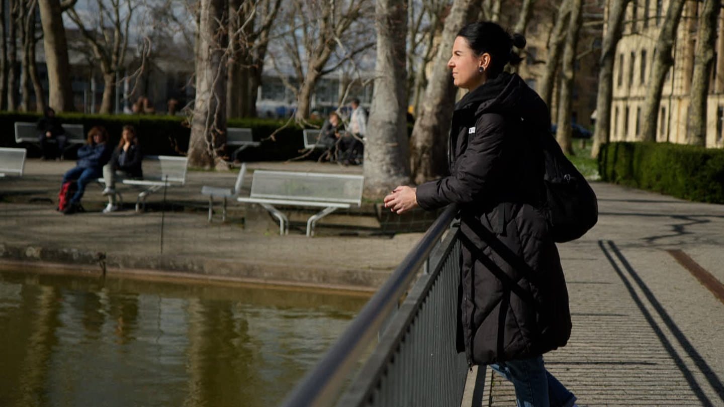 Sina Frehner steht auf einer Brücke auf dem Gelände der Uniklinik Freiburg und schaut nachdenklich in den Teich vor ihr. (Foto: SWR)