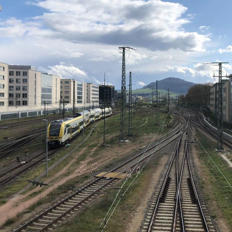 Blick auf den Schönberg, im Vordergrund liegen viele Zuggleise. Auf einem fährt ein gelber Zug, der Breisgau-S-Bahn.