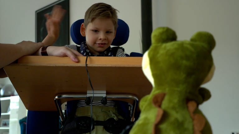 Linus und ein Stofftier-Krokodil. Das Kind mit Förderbedarf übt einen Knopf zu drücken.