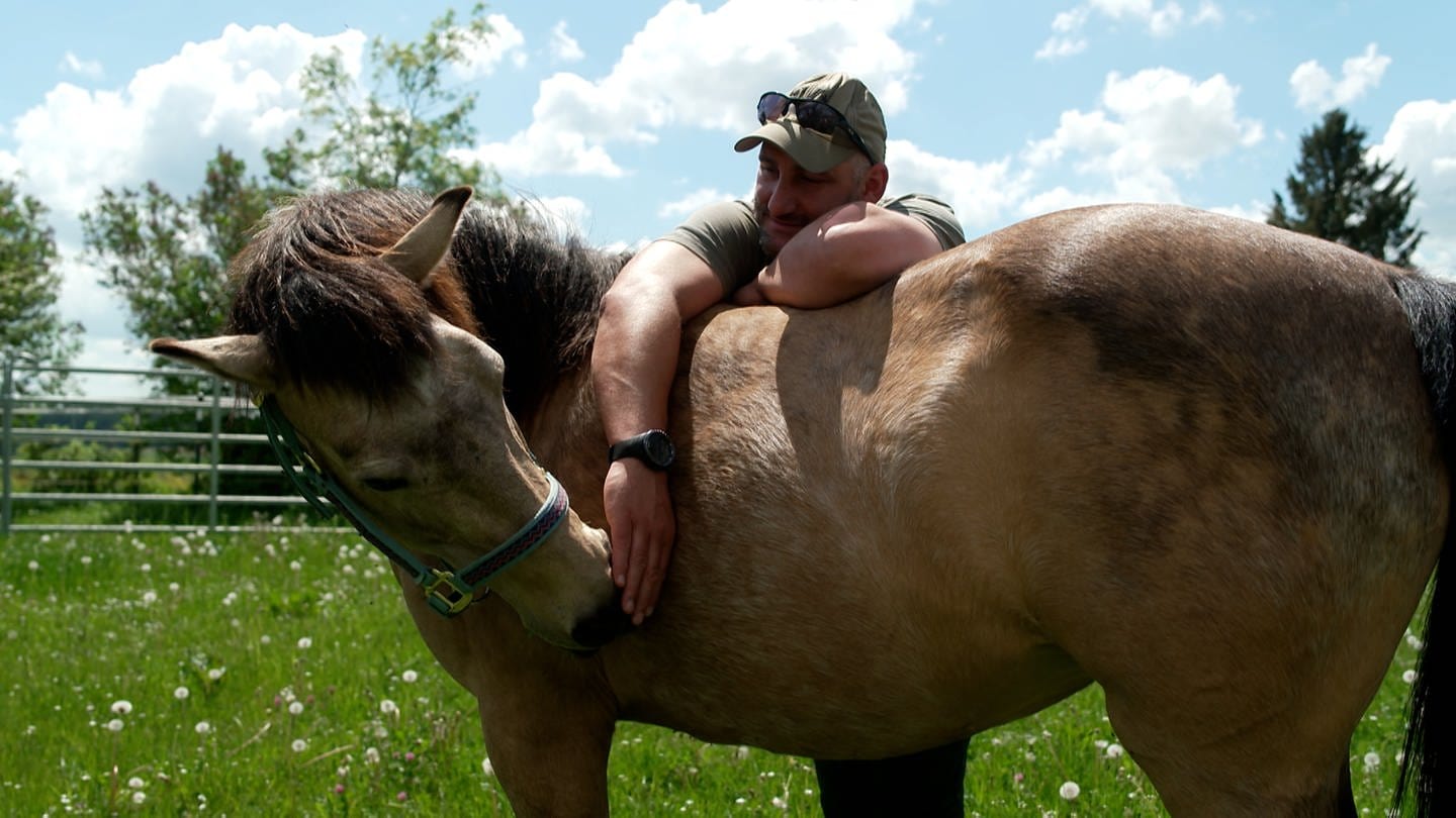 Ein Mann lehnt an einem Pferd - Pferde werden in Aichhalden eingesetzt, um Soldaten zu therapieren (Foto: SWR)