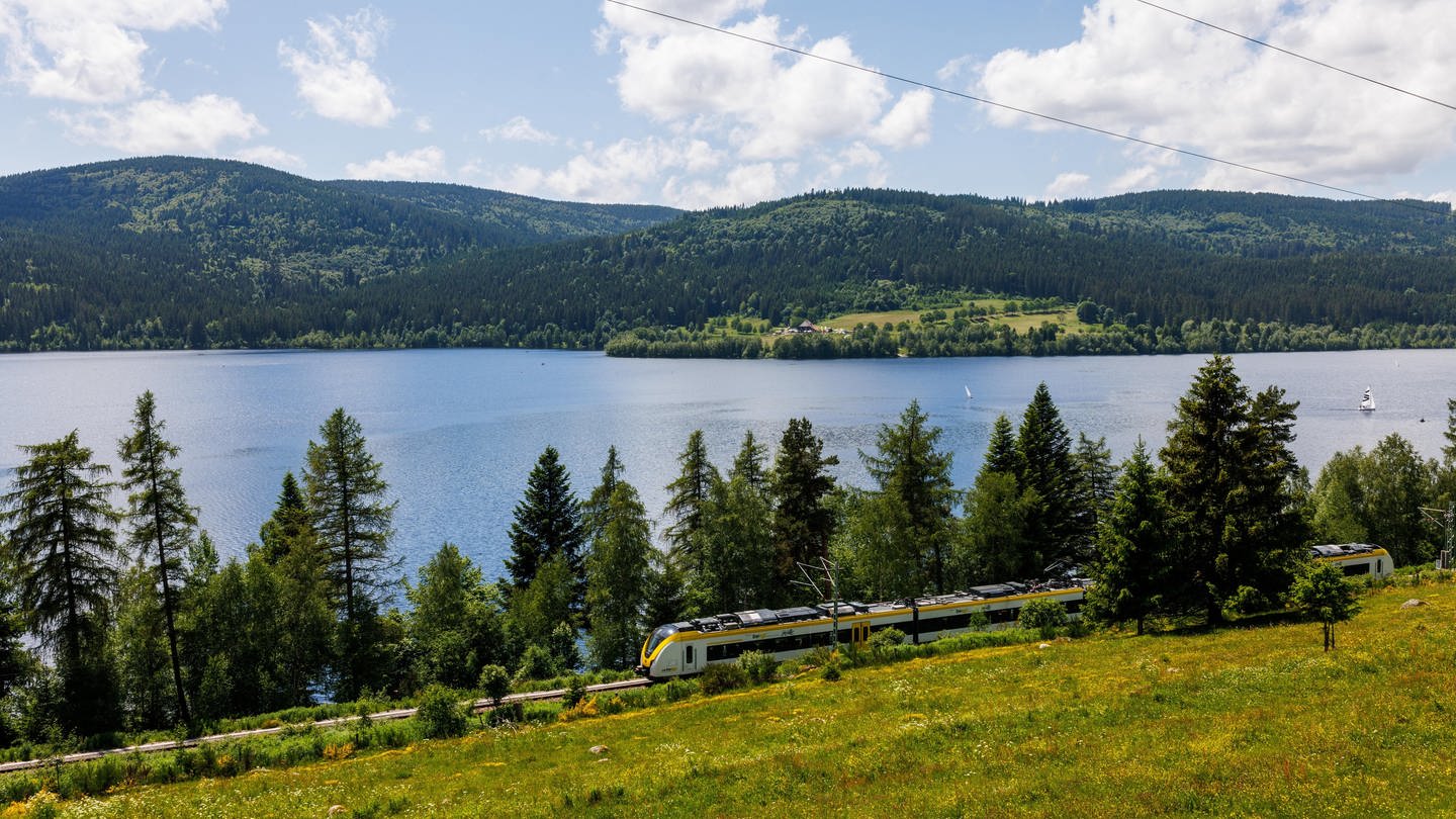 Neben einem großen blauen See, dem Schluchsee, liegen Schienen. Auf diesen fährt ein gelber Dieselzug. (Foto: picture-alliance / Reportdienste, picture alliance / dpa / Philipp von Ditfurth)