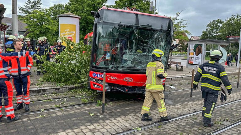 Ein Bus hat eine völlig zerstörte Windschutzscheibe und liegt zurm Teil auf einem Straßenbahn-Gleis.