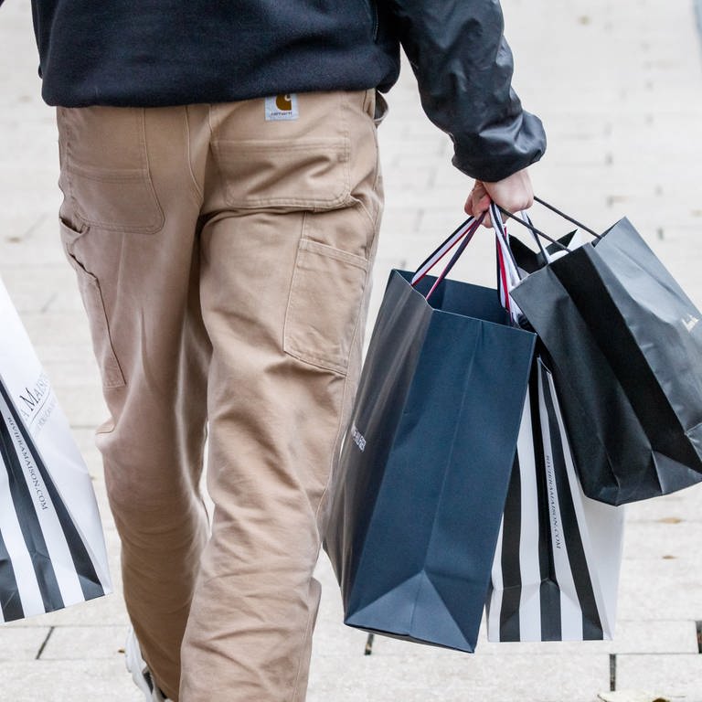 Ein Mann trägt mehrere Einkaufstüten von einem erfolgreichen Shoppingtag, Einkaufstag. Von der Person ist die untere Körperhälfte von hinten zu sehen. (Foto: dpa Bildfunk, dpa Bildfunk - Markus Scholz)