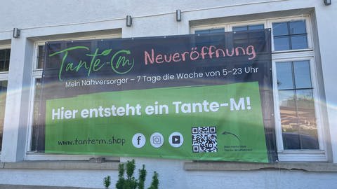 Ein Banner hängt an der Fassade des zukünftigen Tante-M-Ladens in Rottenburg-Kiebingen. Darauf wird die Eröffnung angekündigt. (Foto: SWR, Theresa Krampfl)