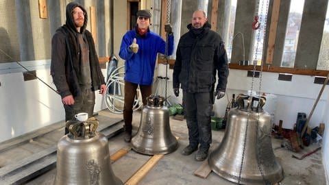 Projektleiter Johannes Längle mit Mitarbeitern der Glockengießerei Bachert stehen hinter drei neuen Kirchenglocken in Tübingen-Lustnau (Foto: SWR, Sonja Legisa)