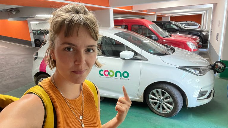 Reporterin Theresa Krampfl steht vor einem E-Auto des Carsharing-Anbieters Coono.  (Foto: SWR, Theresa Krampfl)