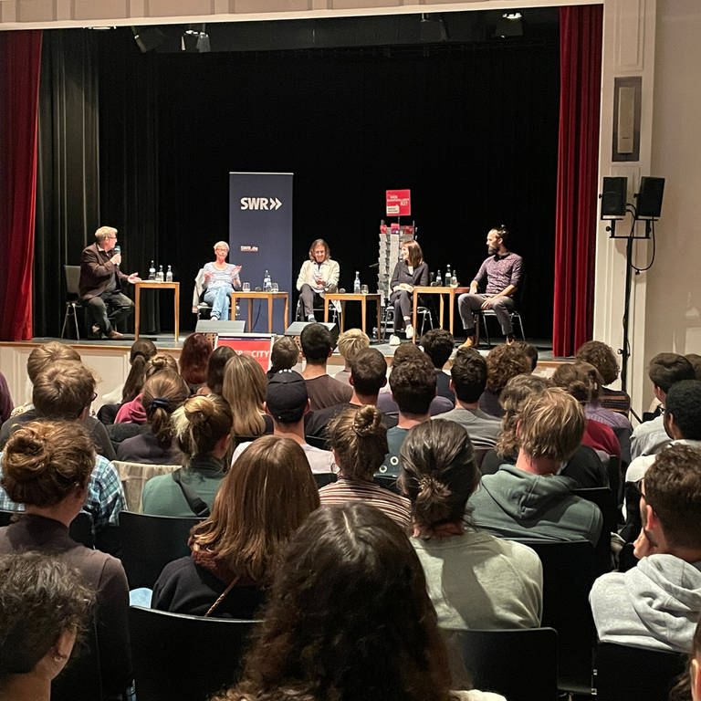 Auf dem Podium in Tübingen sitzen Wissenschaftler und diskutieren über Künstliche Intelligenz. Viele junge Menschen sitzen im Publikum. (Foto: SWR)