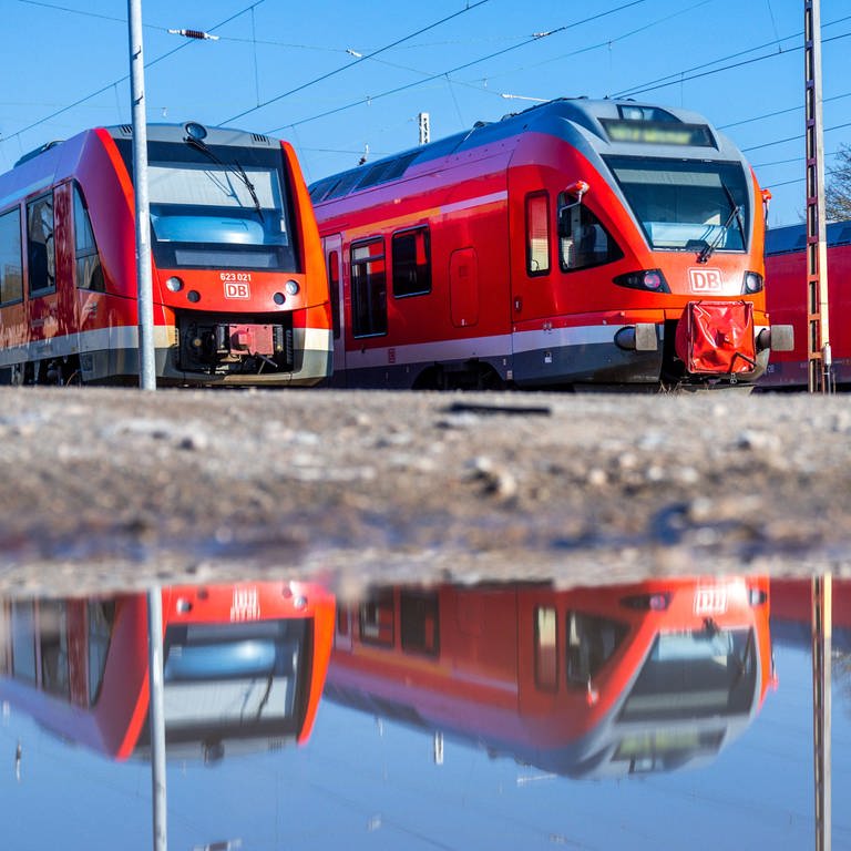 Personenzüge der Deutschen Bahn (DB) stehen auf Abstellgleisen und spiegeln sich in einer Pfütze. Mit bundesweiten Warnstreiks werden Teile des öffentlichen Verkehrs lahmgelegt. (Foto: dpa Bildfunk, picture alliance/dpa | Jens Büttner)