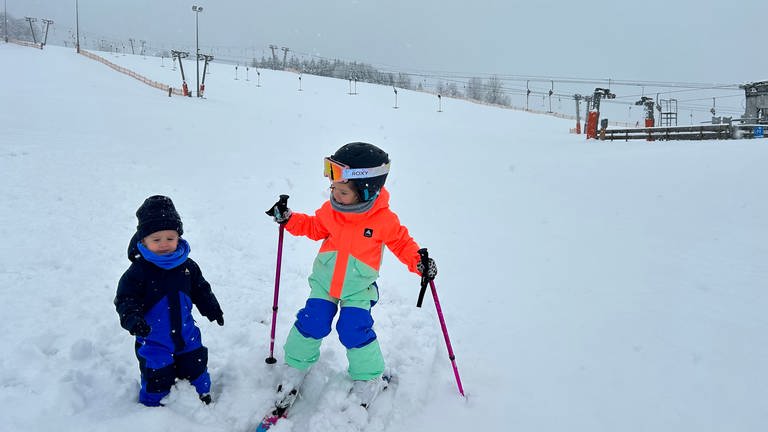 Zwei Kinder im Schnee, eines auf Skiern, im Hintergrund ein Skilift (Foto: SWR, Anne Schmidt)