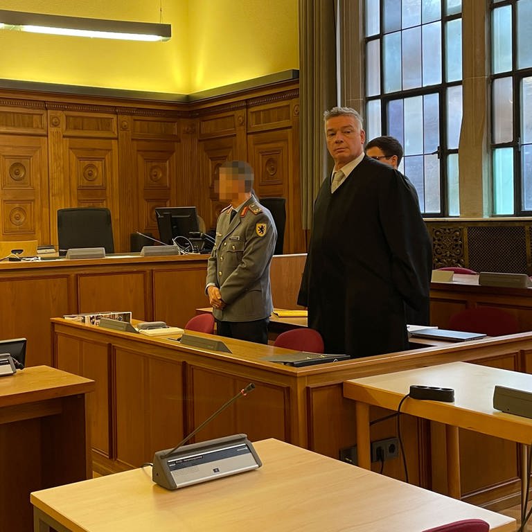 Ex-Brigadegeneral Markus Kreitmayr stehend im Gerichtssaal des Landgerichts Tübingen mit Blick auf den Richter. Rechts neben ihm sein Verteidiger Bernd Müssig, der in den Zuhörerbereich schaut. (Foto: SWR, Priese, Anna)