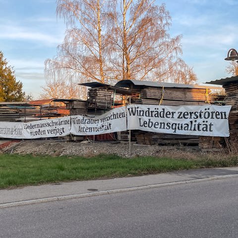 Ein Protestplakat gegen Windräder hängt neben einem Holzlager in Starzach, Kreis Tübingen. In Starzach wird ein Windpark mit sieben Windrädern geplant. (Foto: SWR, Ingemar Koerner)