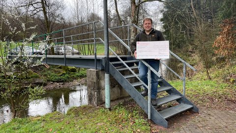 Jan Blötscher steht auf einer Stufe der Brücke über die Glatt. In seiner Hand hält er den Scheck.  (Foto: SWR, Ingemar Koerner)