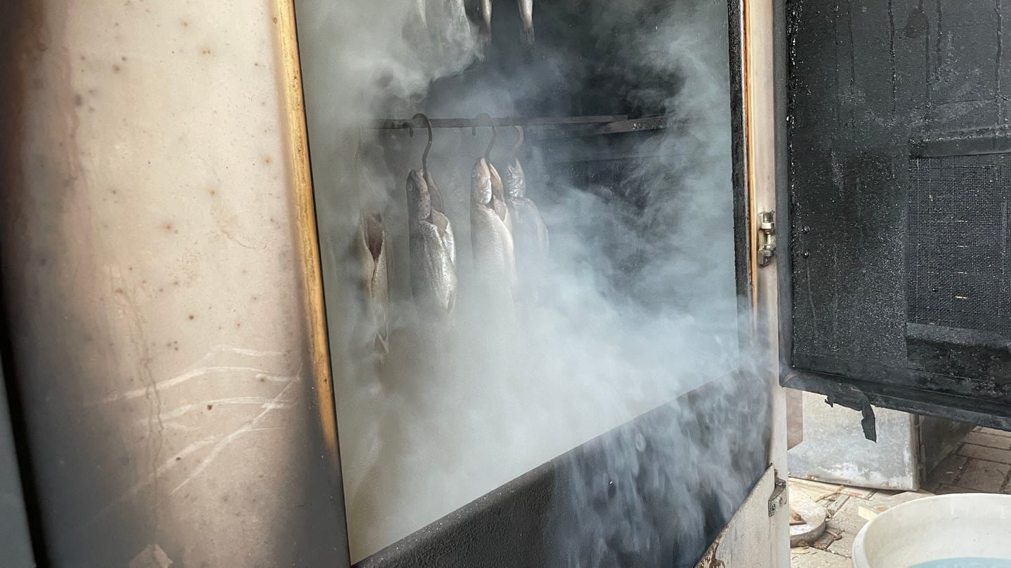 Frische Forellen hängen in einem Räucherofen. Die Ofentür steht offen, der Rauch kommt raus. (Foto: SWR, Ingemar Koerner)