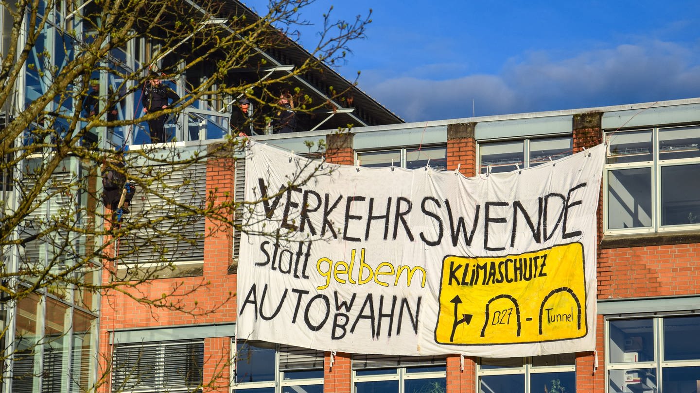 Protestplakat am Regierungspräsidium in Tübingen mit der Aufschrift: Verkehrswende statt gelbem Auto WB ahn. Mitglieder der Klimaaktivistinnen Tübingen klettern am 04.04.2024 auf das dach des Regierungspräsidiums und besfestigen ein Plakat als Protest gegen den Neubau eines B27 Tunnels (Foto: Klimaaktivistinnen Tübingen)