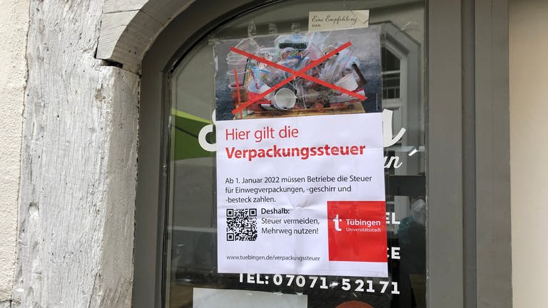 Ein Plakat der stadt Tübingen, angebracht auf einem Schaufenster, mit der Aufschrift "Hier gilt die Verpackungssteuer"