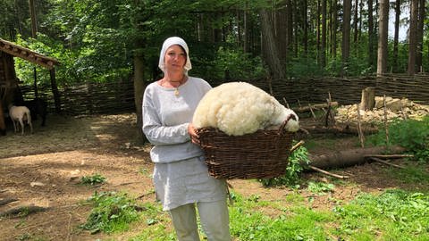 Tierpflegerin Malin trägt das Schaffell in einem Weidenkorb nach der Schur in die Weberei (Foto: SWR)