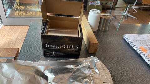 Ein Päckchen Alufolie von "First Foils" steht auf dem Tresen des Tübinger Friseurs. Er verwendet seit kurzem nachhaltige Folie zum Färben. (Foto: SWR, Sarah Beschorner)