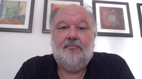 Bildschirmfoto eines ernst blickenden Mannes mit weißgrauem Bart 