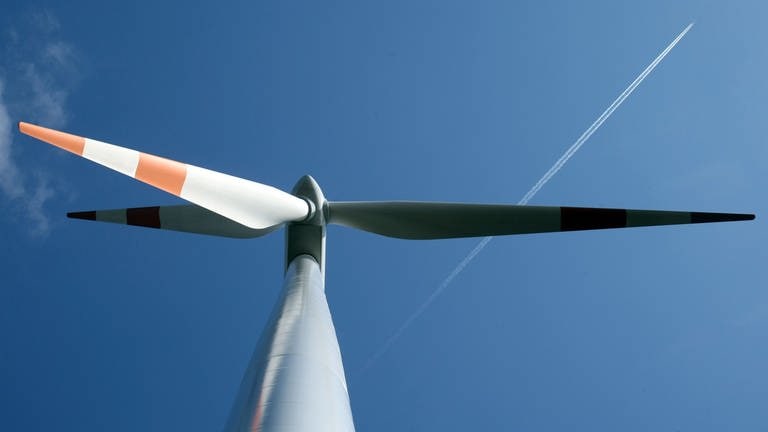 Eine Windkraftanlage von unten vor einem blauen Himmel. Dort fliegt ein Flugzeug in Richtung der rechten, oberen Bildecke. (Foto: dpa Bildfunk, Uli Deck)