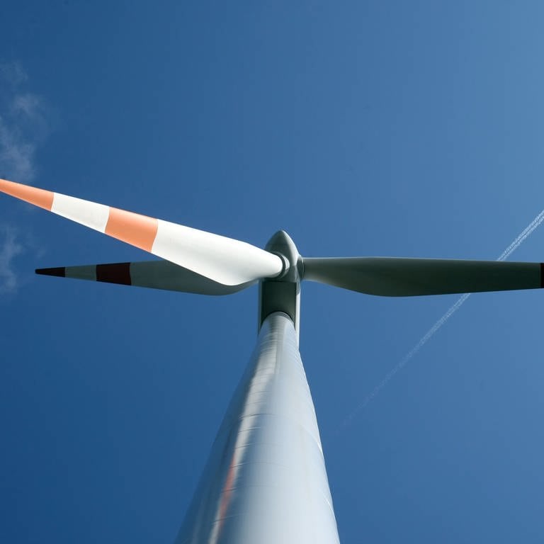 Eine Windkraftanlage von unten vor einem blauen Himmel. Dort fliegt ein Flugzeug in Richtung der rechten, oberen Bildecke. (Foto: dpa Bildfunk, Uli Deck)