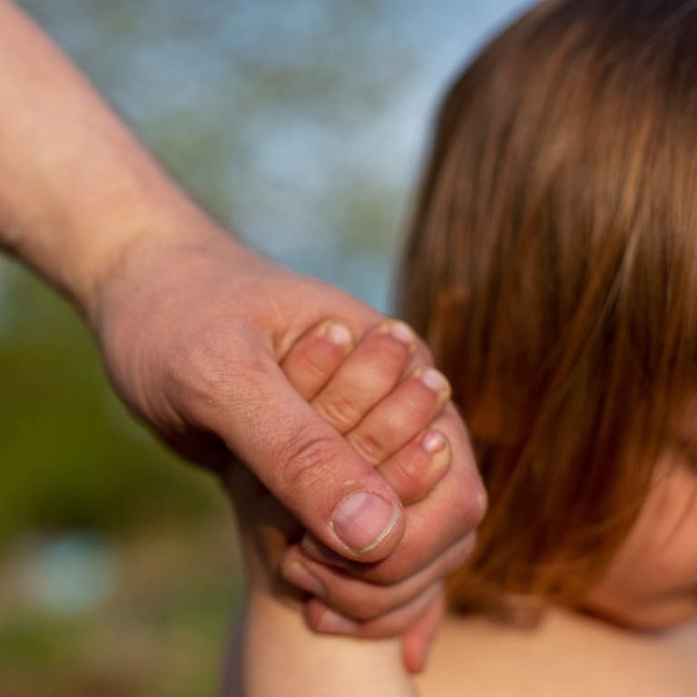 Eine Männerhand hält eine Kinderhand, unscharf dahinter ein kleines Kind mit langen Haaren erkennbar.  (Foto: dpa Bildfunk, Fernando Gutierrez-Juarez)