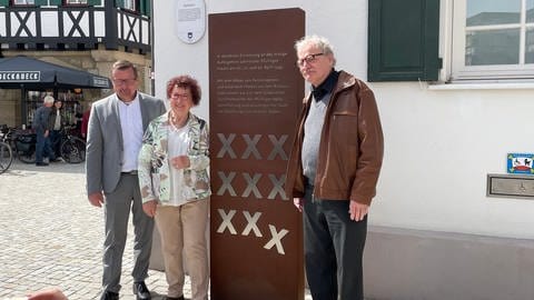 Bürgermeister, First Lady Baden Württembergs und Grafiker stehen zufrieden vor der neuen rechteckigen und übermannshohen Stele vor dem Pfullinger Rathaus. (Foto: SWR, Mia Zundel)