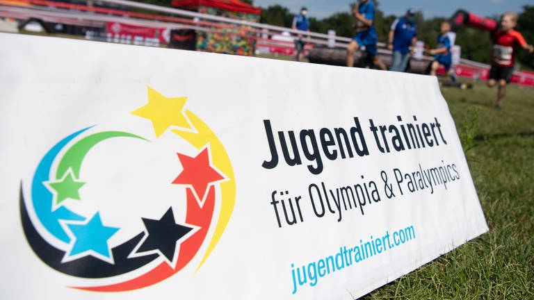Jugendliche rennen an Schild mit Aufschrift "Jugend trainiert für Olympia" vorbei. (Foto: dpa Bildfunk, picture alliance/dpa | Paul Zinken)