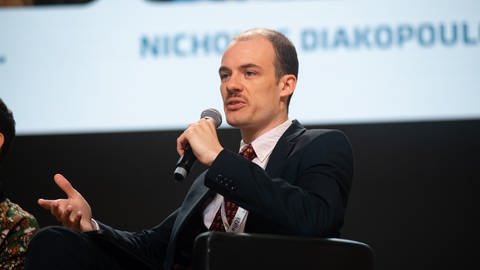 Felix Simon in Anzug und Krawatte auf dem Podium einer öffentlichen Veranstaltung (Foto: Pressestelle, creativecommons)
