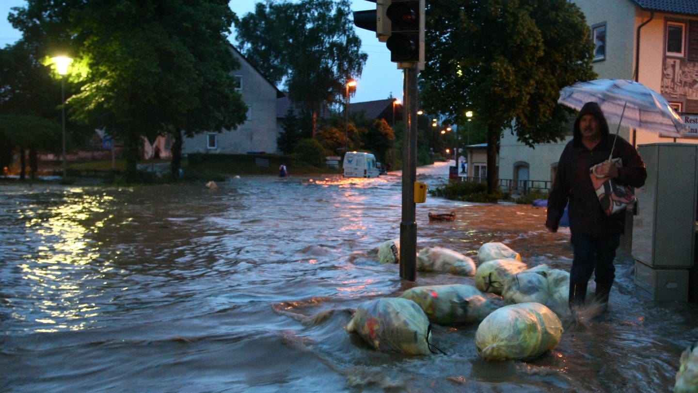 Hochwasser Killertal Rückblick, Mann mit Regenschirm läuft auf überfluteter Straße zwischen schwimmenden Müllsäcken (Foto: dpa Bildfunk, picture-alliance/ dpa | Marc Müller)