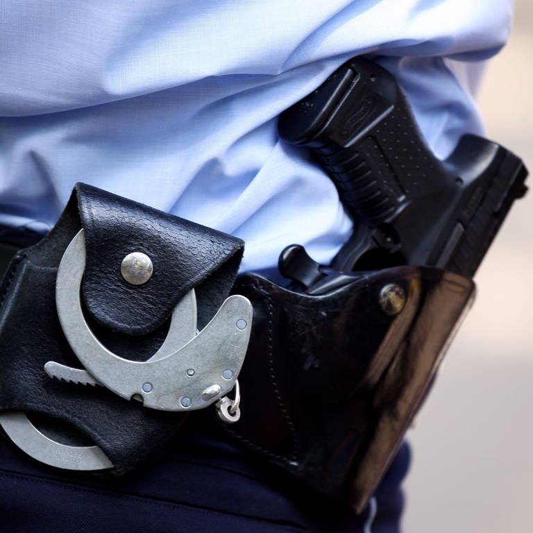 Ein Polizist trägt Handschellen und seine Dienstwaffe bei sich. 23 Jahre nach einem Mafiamord in Italien ist ein mutmaßlicher Täter in Baden-Württemberg gefasst worden. (Foto: dpa Bildfunk, Picture Alliance)
