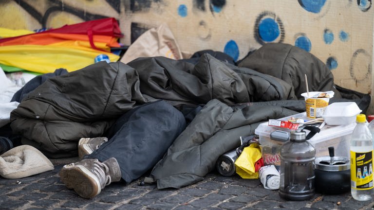 Eine Person liegt in der Innenstadt unter einem Schlafsack.